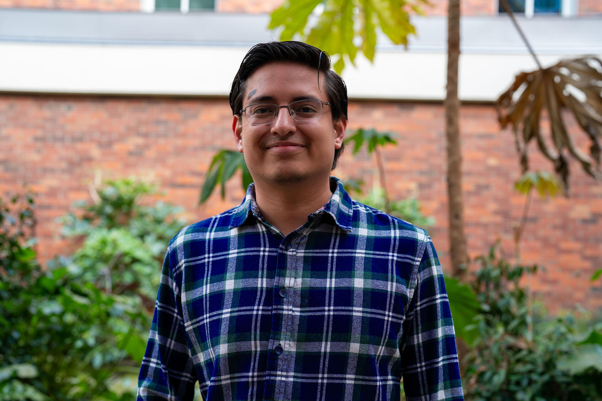 Jose posing for the camera in front of a brickwall and bushes
