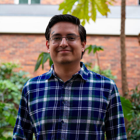 Jose posing for the camera in front of a brickwall and bushes